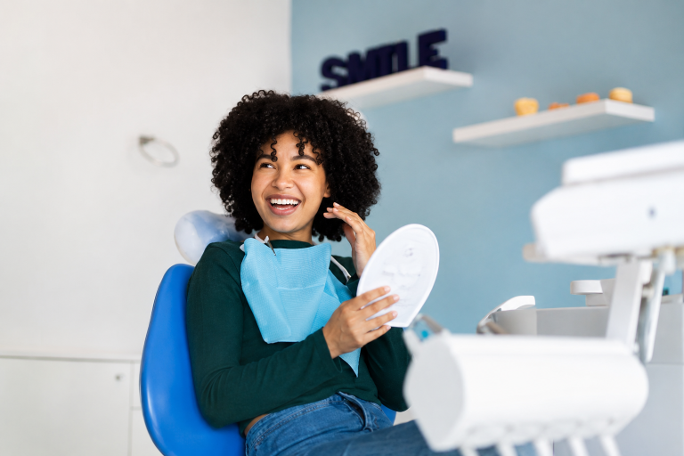 Smiling patient holding a mirror in a modern dental clinic after a dental visit